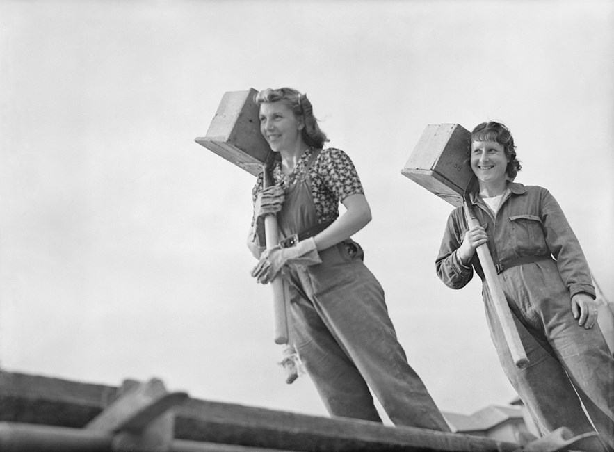 Two female builders carry hods of bricks on a building site, 1941 © Imperial War Museum. Source: https://www.historicengland.org.uk/news-and-features/news/england-built-by-women